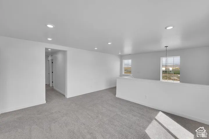 Spacious carpeted area with recessed lighting, multiple windows, and a black-finish chandelier