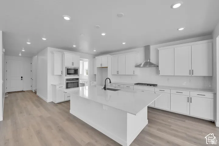 Open-concept kitchen featuring an expansive island with a matte black faucet, white cabinetry, integrated stainless steel appliances, and wood-finish flooring