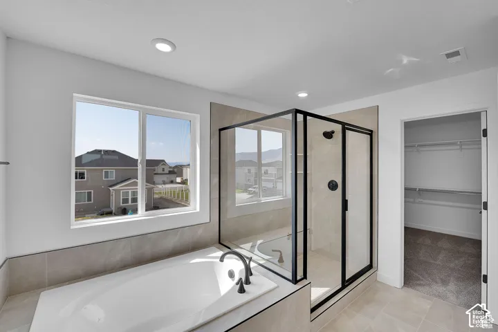 Built-in soaking tub with a black faucet, glass-enclosed shower with black hardware, recessed ceiling lighting, and a walk-in closet with shelving