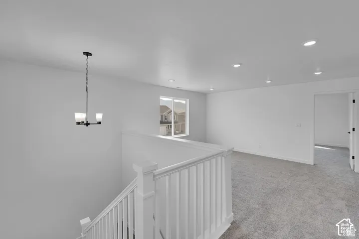 Carpeted landing with a white painted railing, recessed ceiling lighting, and a modern chandelier