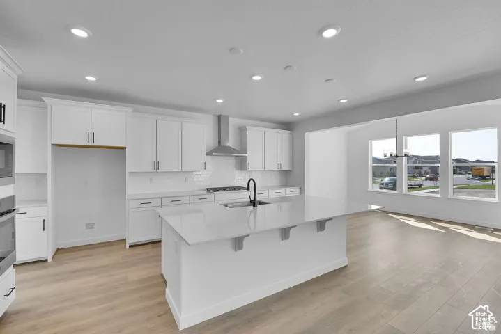 Kitchen featuring an expansive island with a solid surface countertop, white cabinetry with modern hardware, subway tile backsplash, and wood-finish flooring