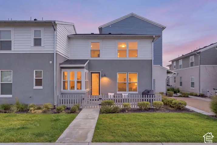 Modern two-story residence featuring a light gray and white exterior with board-and-batten siding, gable roofline, and expansive front-facing windows with warm interior lighting