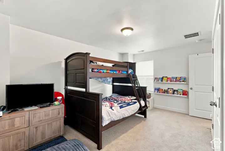 Spacious bedroom featuring a dark wood bunk bed with built-in storage shelving, neutral carpeting, recessed ceiling lighting, and coordinating wood-finish dresser with integrated television placement