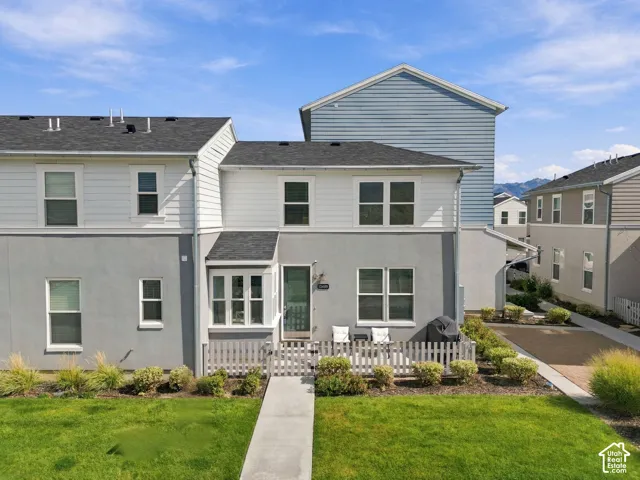Modern townhome exterior with mixed material siding, fenced front patio, and a grass lawn