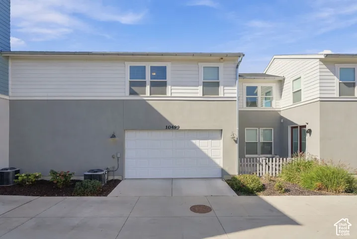 Modern townhome featuring a two-car garage with white paneled door, concrete driveway, and neutral exterior finishes in cream and gray tones