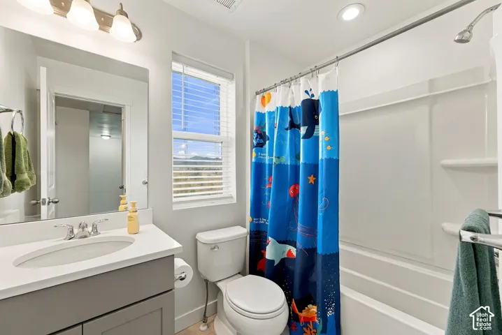 Bright and updated bathroom featuring a gray vanity with white countertop, large framed mirror, white subway tile surround in the shower area, chrome fixtures, and abundant natural light from a multi-pane window