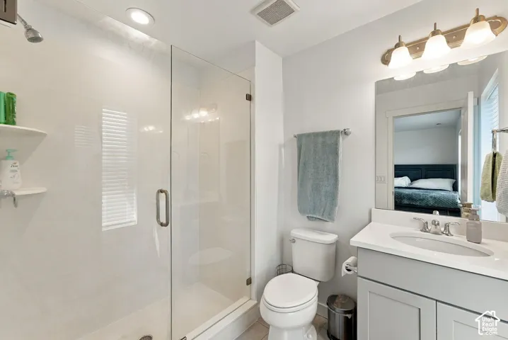 Modern bathroom featuring a frameless glass-enclosed shower with tile surround, white vanity with dual sink configuration and brushed nickel fixtures, porcelain toilet, and brass-finish overhead lighting