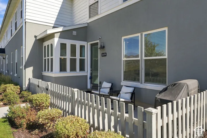 Private patio area featuring a light-toned picket fence, gray stucco exterior, and a large bay window
