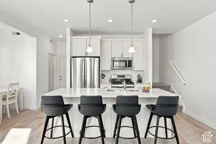 White cabinetry with stainless steel appliances, a large center island, recessed lighting, and wood-finish flooring