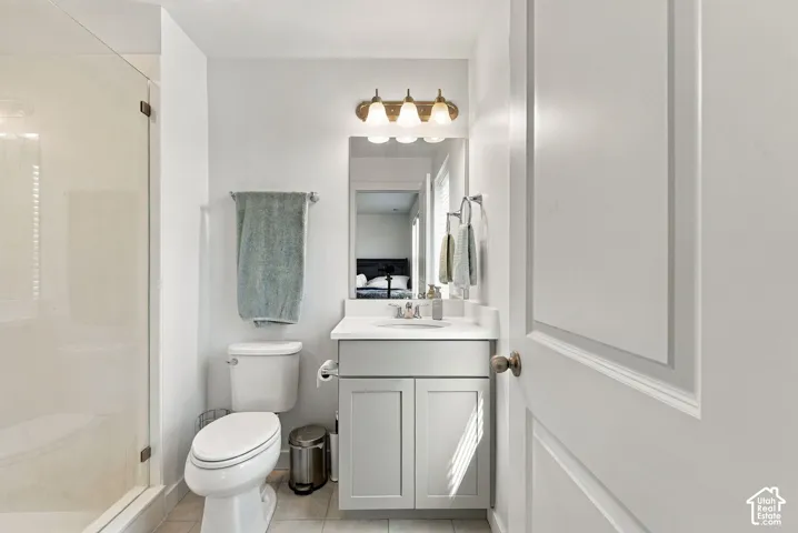 Glass-enclosed shower, white toilet, single vanity with light gray cabinetry, white countertop, and three-light vanity fixture