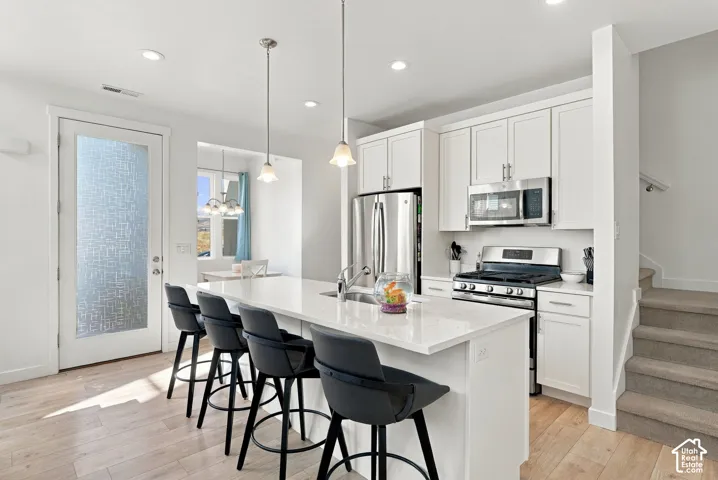 Kitchen featuring a large island with sink, stainless steel appliances, white cabinetry, and recessed lighting