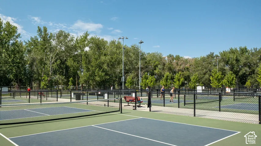 Multiple outdoor courts with blue and green surfaces, black perimeter fencing, and mature trees