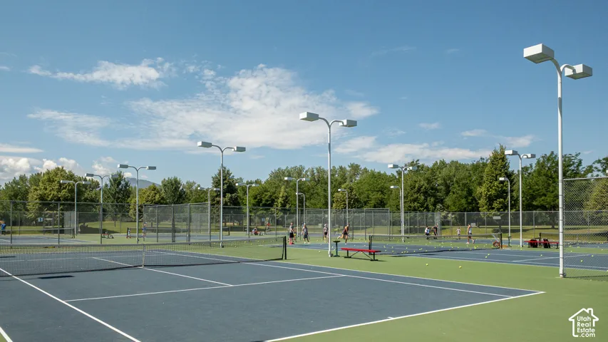 Multiple tennis courts with blue and green surfacing, surrounded by chain-link fencing, and illuminated by multiple light poles