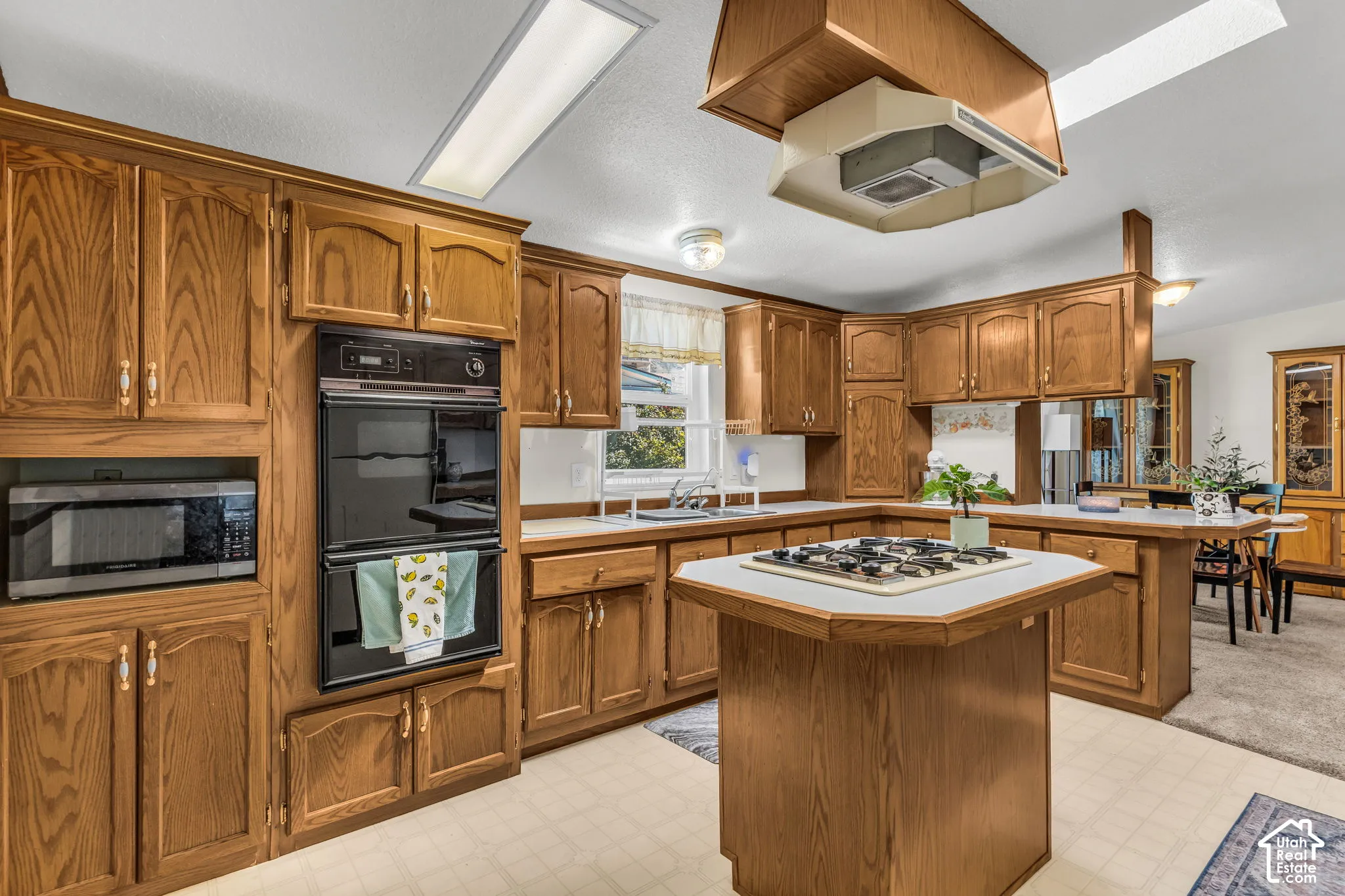 Kitchen featuring extensive wood cabinetry, built-in double oven, integrated microwave, and a central island with a cooktop