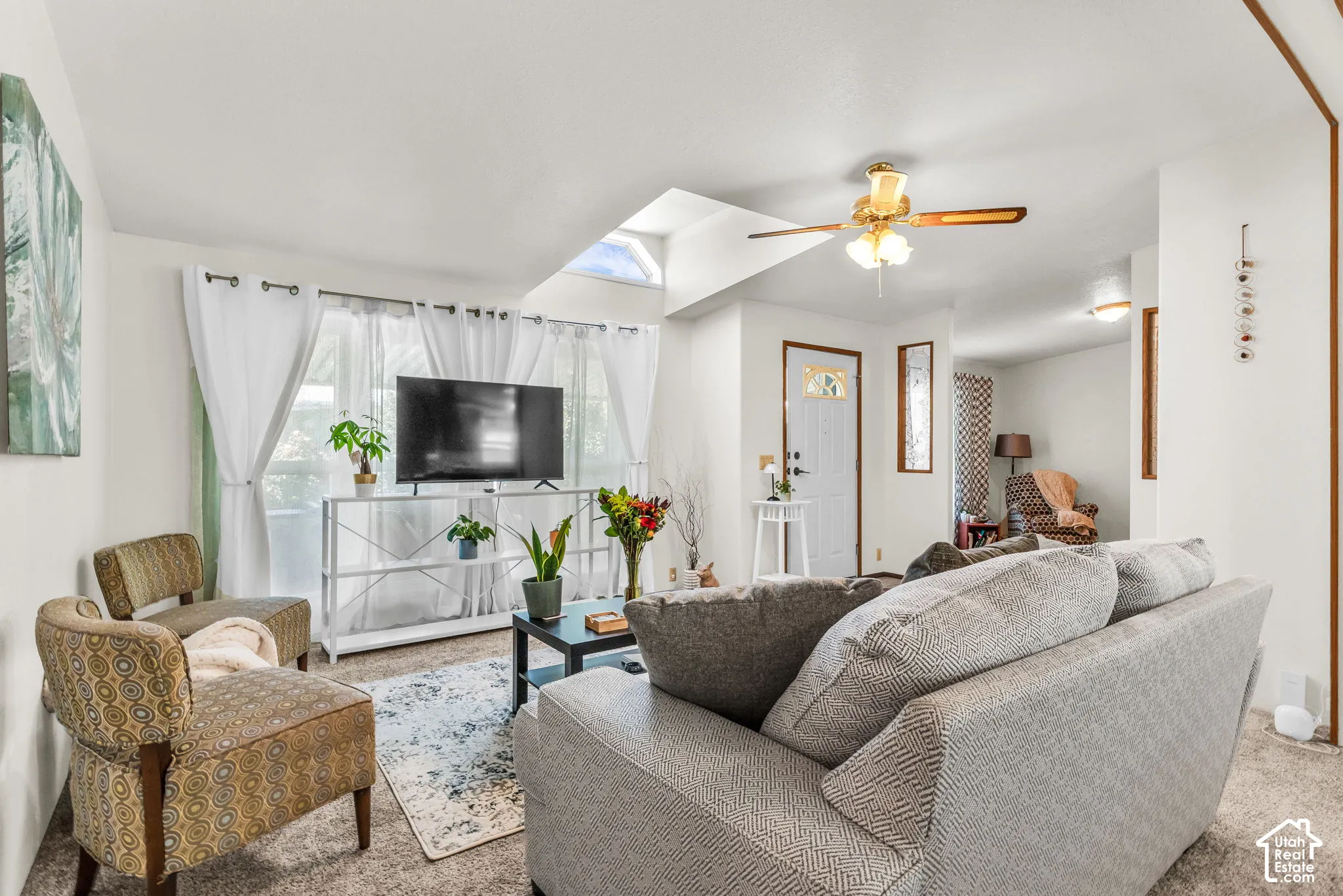 Vaulted ceiling with skylight and ceiling fan, carpeted flooring, and a white paneled entry door with decorative glass