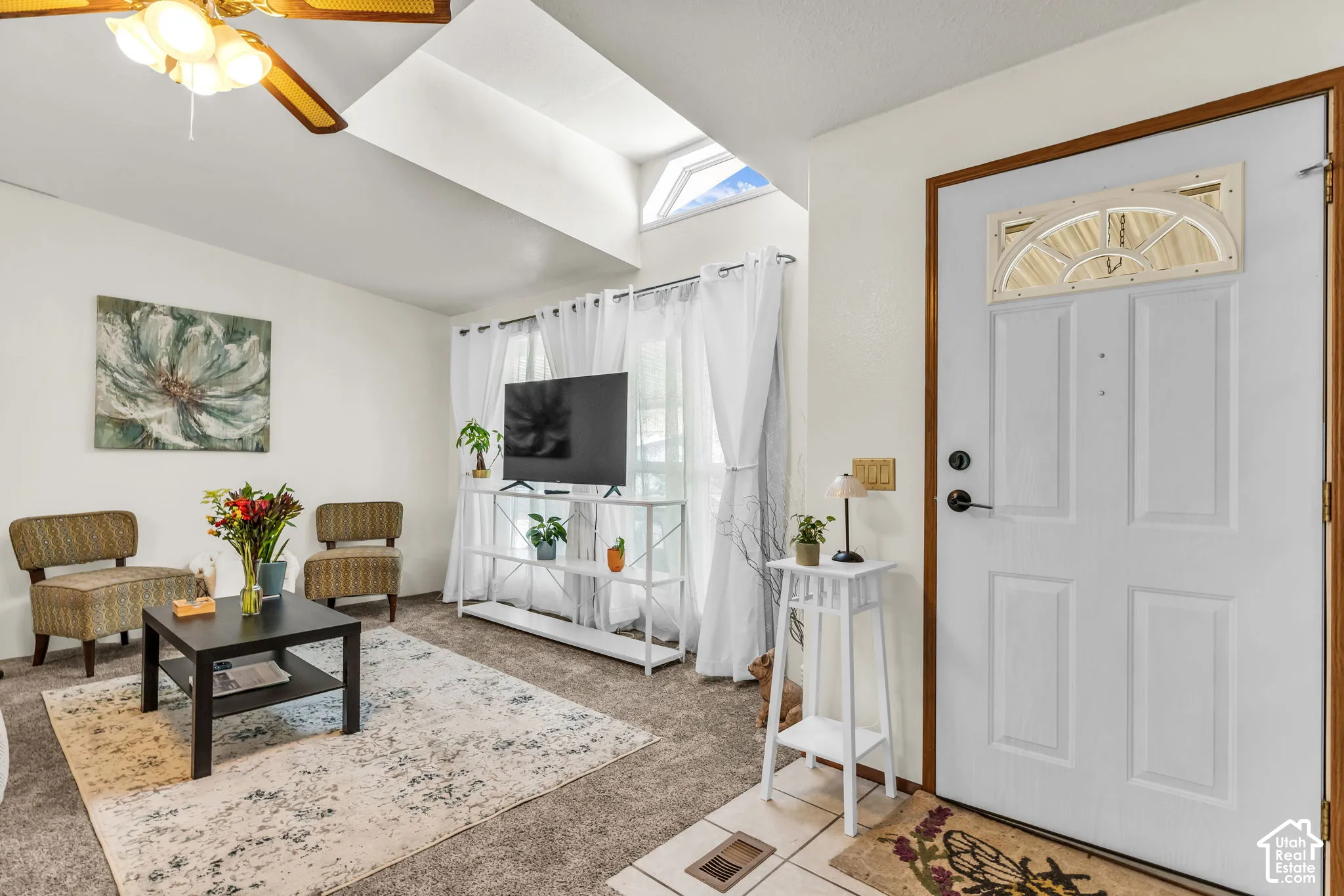 Vaulted ceiling with skylight and ceiling fan, white paneled entry door with transom window, and tiled entry flooring