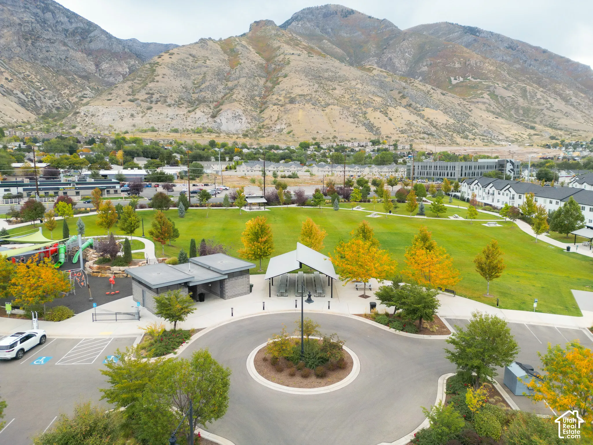 Expansive park with manicured lawns, mature trees, playground structures, and a dedicated parking area