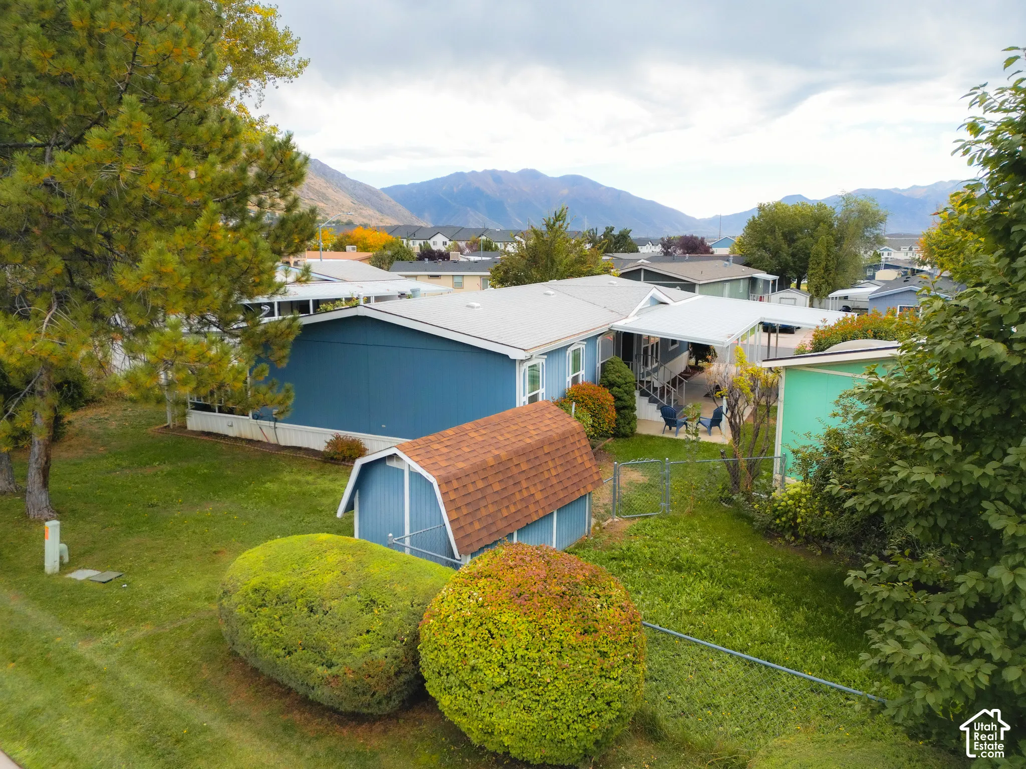 Expansive yard with mature trees, a blue storage shed with a shingle roof, and a mountain backdrop