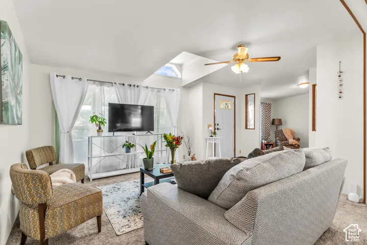 Vaulted ceiling with skylight and ceiling fan, carpeted flooring, and a white paneled entry door with decorative glass