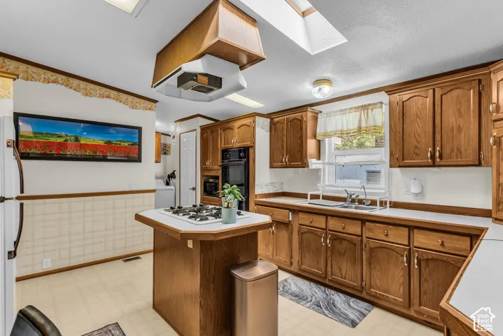 Kitchen featuring wood-finish cabinetry, a built-in oven, a center island with a gas cooktop, and a skylight