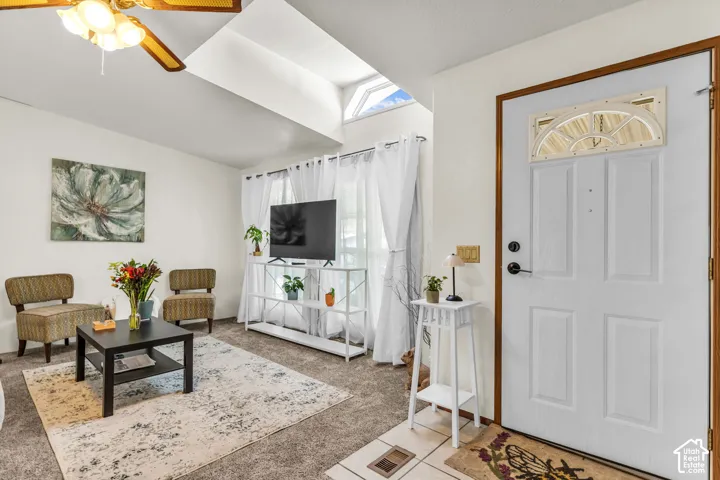 Vaulted ceiling with skylight and ceiling fan, white paneled entry door with transom window, and tiled entry flooring