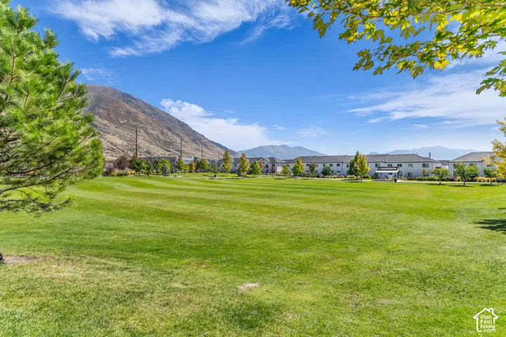 Expansive green space featuring manicured lawn, established trees, and mountain scenery