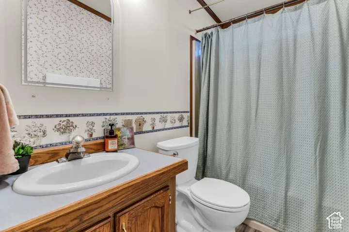 Vanity with a wood-finish base cabinet and laminate countertop, integrated sink basin, wall-mounted mirror, and a toilet