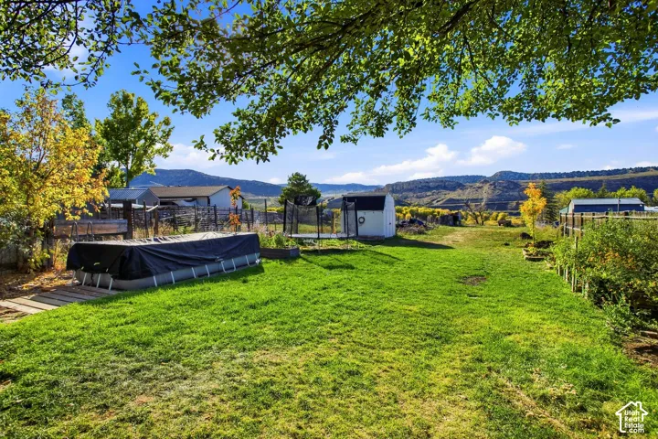 Expansive green lawn with a covered above-ground pool, a white storage shed, and distant mountain scenery