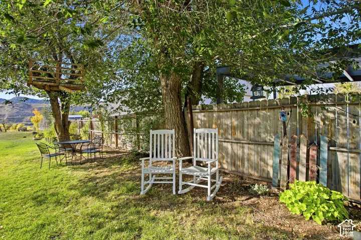 Expansive grassy yard with mature trees, a wooden treehouse structure, a wooden privacy fence, and an outdoor seating area