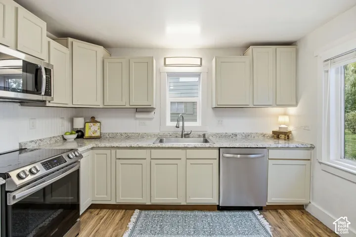 Cream-colored cabinetry with modern hardware, stainless steel appliances, speckled countertops, wood-finish flooring, and a white beadboard backsplash