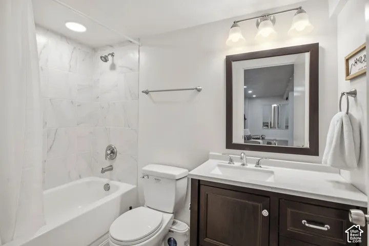 Bathroom featuring a tub/shower combination with white tile surround, a dark wood-finish vanity with a white countertop and integrated sink, and a framed mirror with overhead lighting