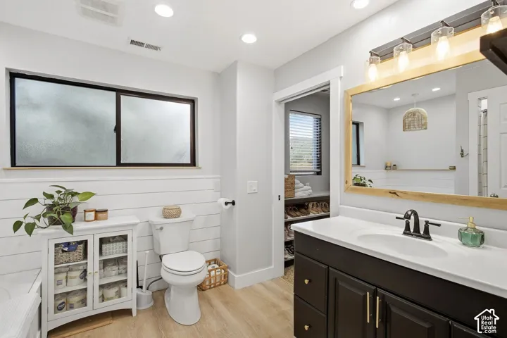 Contemporary bathroom featuring wood-finish flooring, white shiplap wainscoting, a dark vanity with a white countertop, and a large mirror with integrated lighting