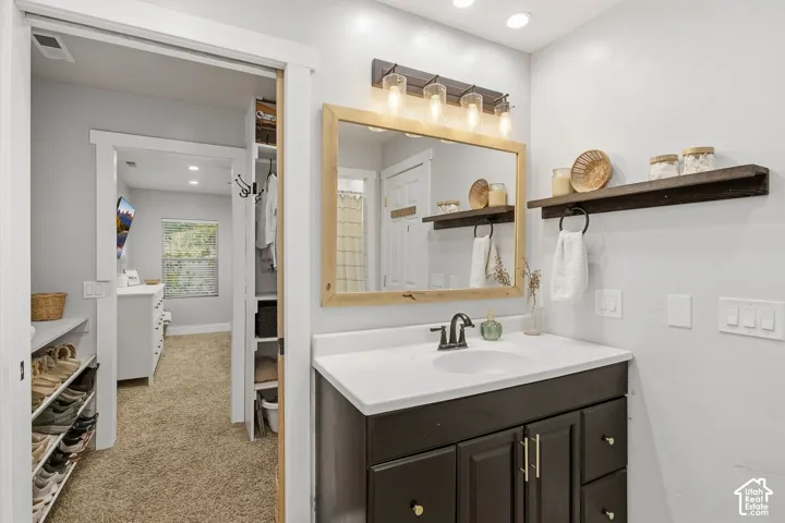Vanity with dark cabinetry and a white countertop, framed mirror with sconce lighting, and floating wood shelving