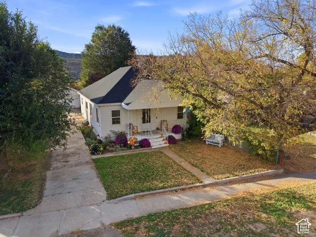 Charming cottage with a gabled roof and covered front porch, set on a landscaped lot featuring mature trees and seasonal plantings