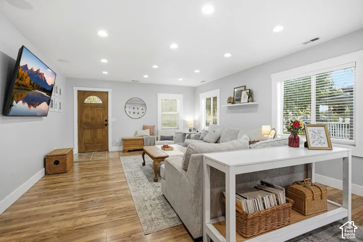 Recessed ceiling lighting, wood-finish flooring, white window trim, and a paneled entry door with an arched glass insert