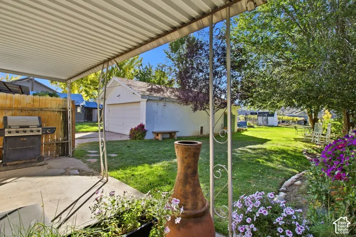 Covered patio area with a concrete slab, a detached garage, a wooden privacy fence, a manicured lawn, and mature trees