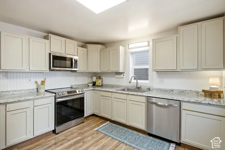 Wood-finish flooring, light-toned cabinetry, stainless steel appliances, stone-look countertops, and a beadboard backsplash