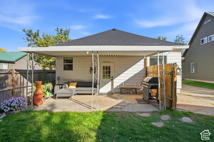 Covered patio area with concrete surfacing, white siding, a dark shingle roof, and a wood privacy fence