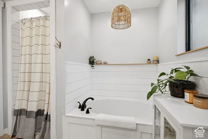 Built-in tub with matte black fixtures, shiplap wall paneling, and a woven pendant light fixture