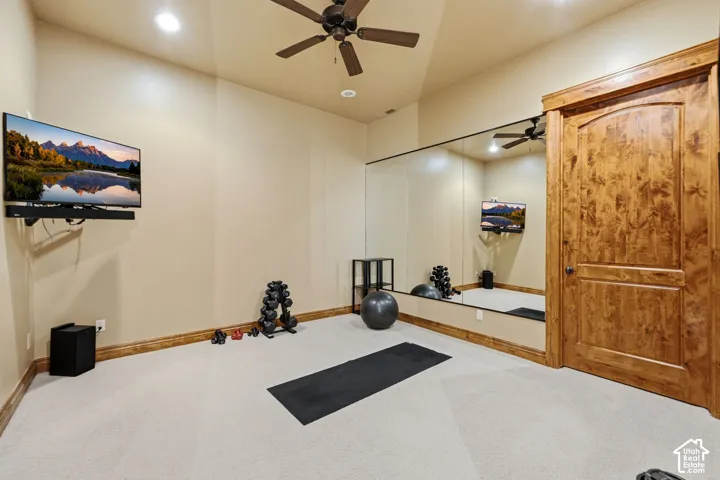 Carpeted room featuring a ceiling fan, recessed lighting, wall-mounted television, and a large mirror wall