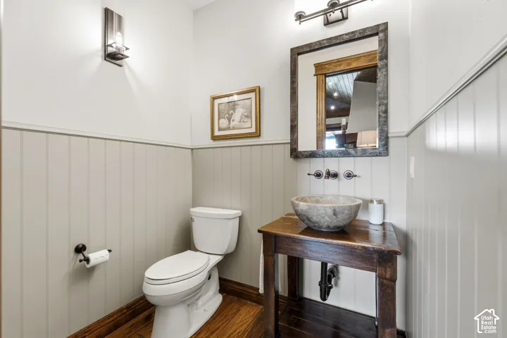 Wood-finish flooring, wainscoting, stone vessel sink, wall-mounted faucet, and wood vanity