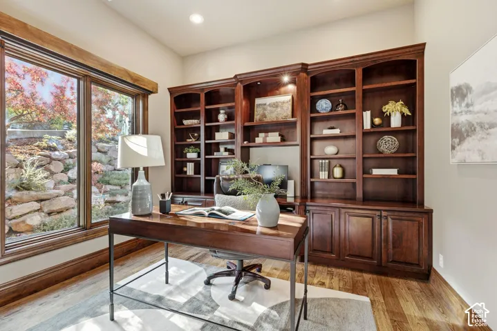 Wood-finish flooring, built-in dark wood cabinetry, large window with wood trim, recessed lighting, and light wall color