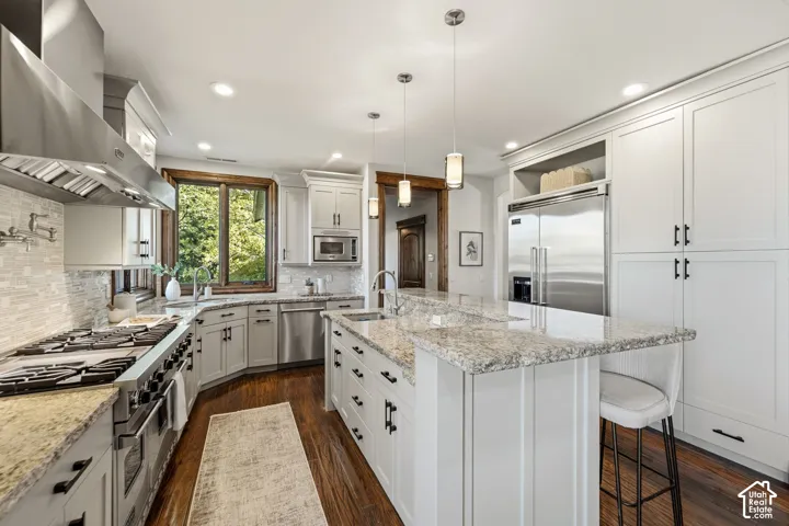 Gourmet kitchen featuring a large island with stone countertops, stainless steel appliances, white cabinetry, hardwood flooring, and a tiled backsplash