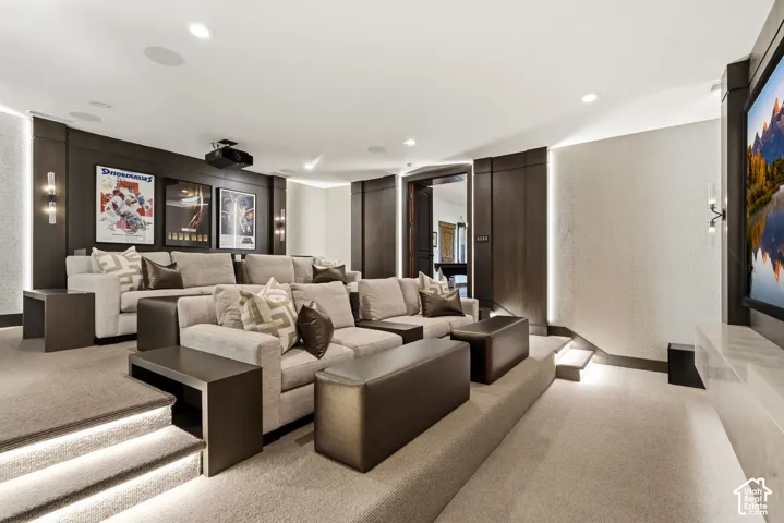 Multi-tiered home theater featuring a large projection screen, recessed ceiling lighting, wall-mounted sconces, and built-in wood paneling