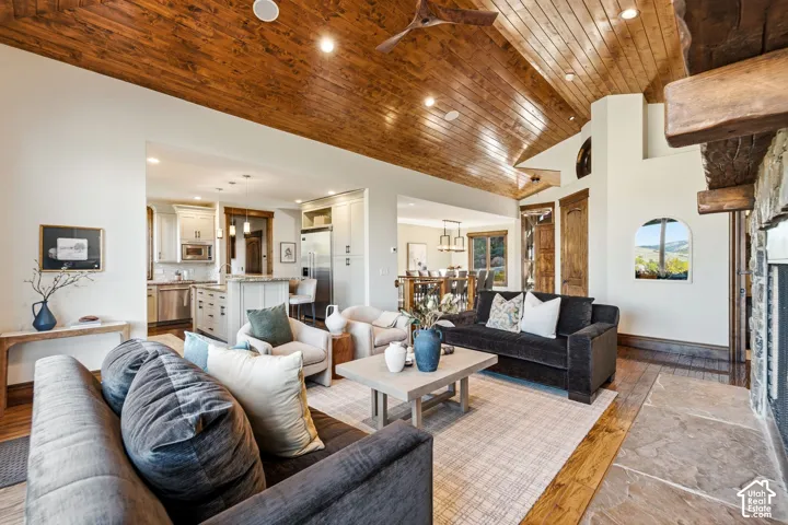 Vaulted wood-paneled ceiling, stone-clad fireplace, wood-finish flooring, recessed lighting, and a kitchen with stainless steel appliances