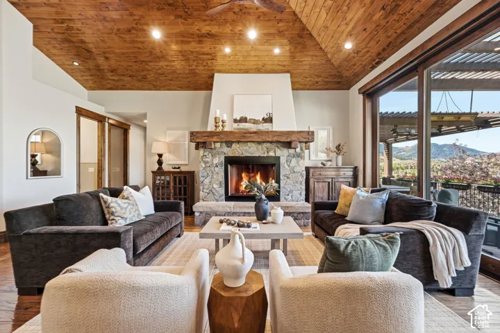 Vaulted wood-paneled ceiling with recessed lighting, stone fireplace with a wood mantel, and large sliding glass doors opening to an exterior balcony