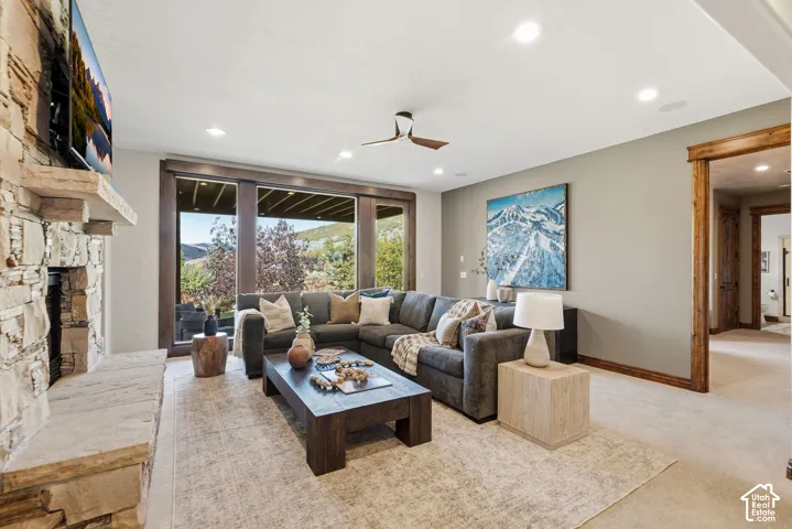 Stone fireplace with a hearth, large windows, recessed lighting, wood-finish ceiling fan, and wood trim around doorways