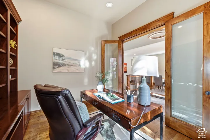Hardwood flooring, recessed ceiling lighting, built-in wooden shelving, and clear glass double doors