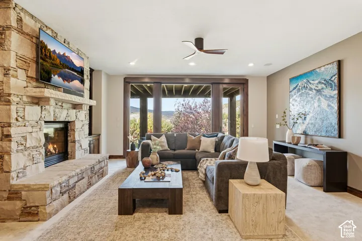 Stone-clad fireplace with hearth, recessed lighting, wood-framed sliding glass doors, and a ceiling fan