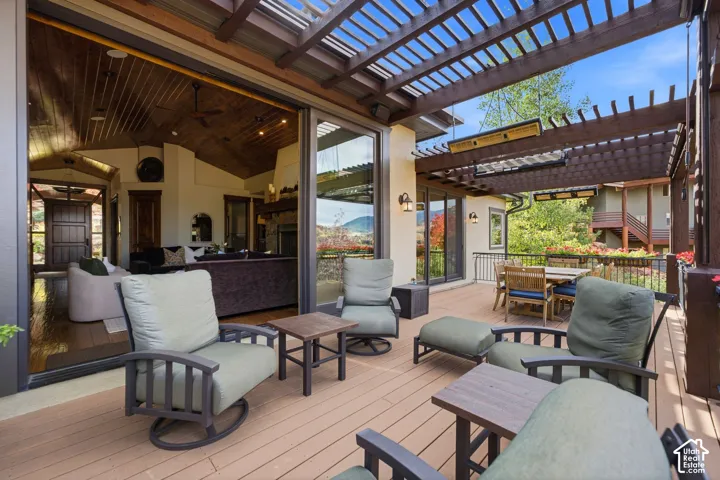 Expansive outdoor deck with a pergola, exterior wall sconces, and sliding glass doors